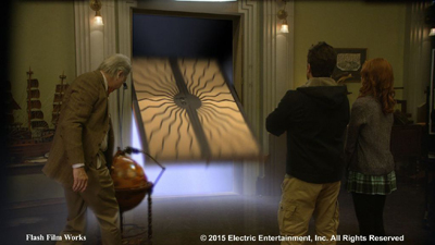 Three people watch a large, glowing, patterned rectangular object pass through a doorway in a dimly lit room.
