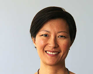 A smiling woman with short dark hair looking at the camera against a light gray background.