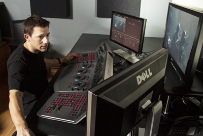 A man sits at a desk using a large control surface and multiple computer monitors in a studio.