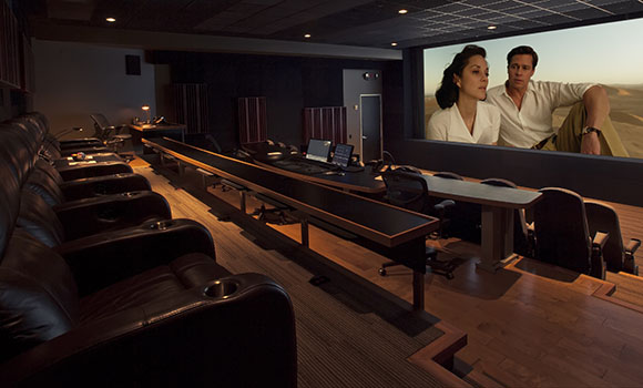 A dark home cinema with rows of black leather recliners facing a large movie screen.