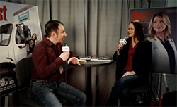 A man in a maroon shirt interviews a woman in a black blazer at a small round table.