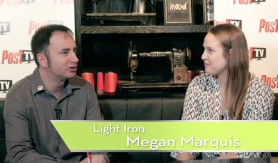 A man in a grey shirt and a woman in a patterned blouse sit talking in front of a dark shelf.