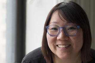 A smiling woman with dark hair and blue-rimmed glasses looking toward the camera.