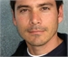 Close-up portrait of a man with dark hair and brown eyes looking directly at the camera.