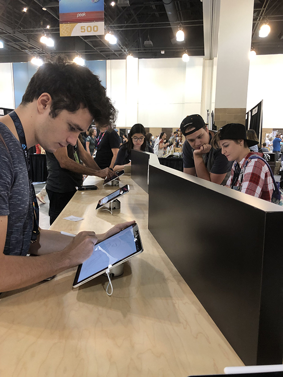 Several people are gathered around a long wooden counter, interacting with tablets displayed on stands. One person in the for