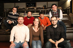 Seven people smiling and posing together in a tiered theater seating area.