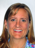 A smiling woman with blonde hair and blue eyes wearing a colorful patterned shirt.
