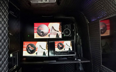 Three screens showing Coca-Cola Zero ads arranged on a desk inside a dark, quilted van interior.
