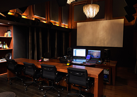 A professional recording studio featuring a large mixing desk, computer monitors, and several black office chairs.