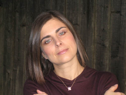 A woman with straight brown hair and light eyes wearing a dark maroon shirt.