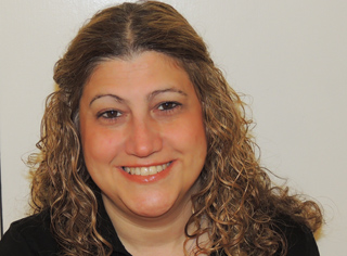 A smiling woman with long, curly light brown hair looking toward the camera.