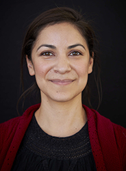 A woman with dark hair pulled back smiles against a dark background.