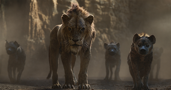 A male lion walks forward in the center, flanked by several hyenas in a dusty environment.