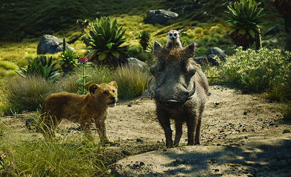 A lion cub, a warthog with a meerkat on its head, and lush greenery in a sunny landscape.