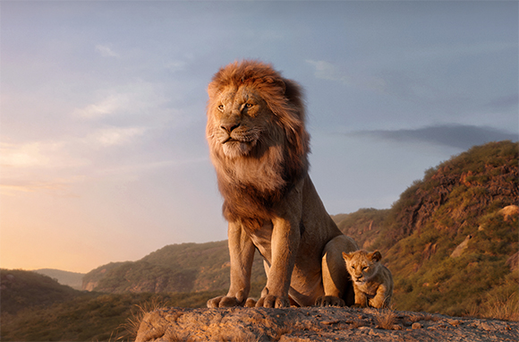 A male lion and a small cub sit atop a rocky outcrop against a soft sunset sky.
