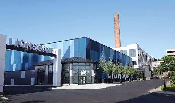 A modern blue and grey building with Lionsgate signage next to a tall brick industrial chimney.