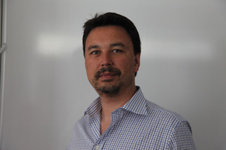 A man with dark hair and a goatee wearing a blue and white checkered button-down shirt.