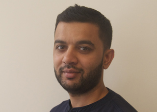 A man with short dark hair and a beard looking forward against a plain light background.
