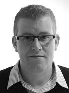 A man with short hair and glasses looking forward against a white background.
