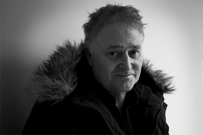 Black and white portrait of a man wearing a dark jacket with a large, fluffy fur hood.