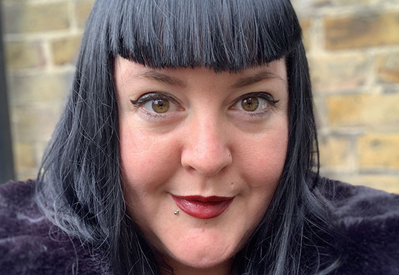 A person with straight black hair, blunt bangs, and dark red lipstick looking at the camera.