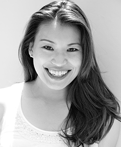 A smiling woman with long dark hair looking towards the camera in a black and white portrait.
