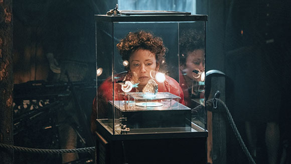 A woman with curly hair gazes intently at an object inside a lit glass display case.