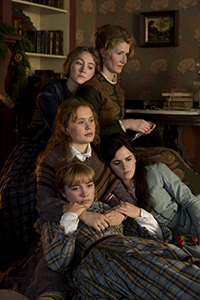 Four young women in 19th-century attire sit closely together in a dimly lit room.