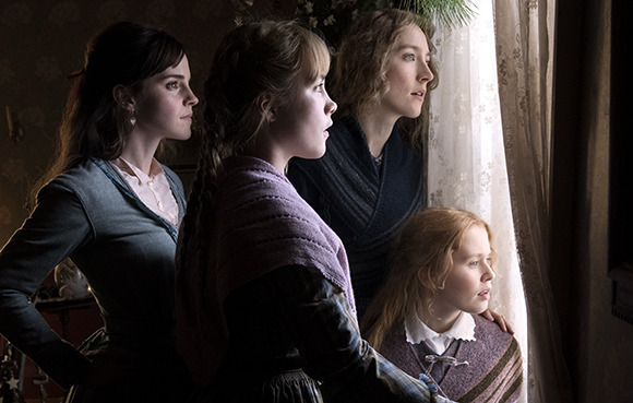 Four women in period clothing gaze intently out of a bright window.