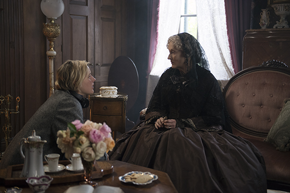 A young blonde woman leans in to talk to an older woman wearing a black lace veil and dress.