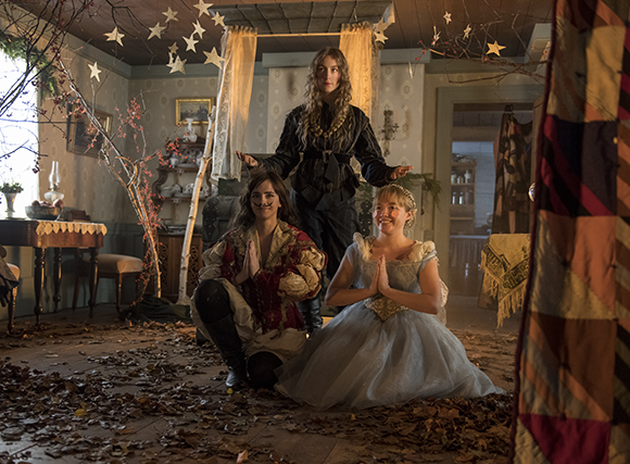 Three women in vintage dresses pose in a room covered in fallen autumn leaves.