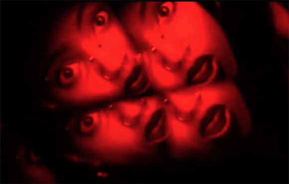 Four faces are shown in a repeating, mirrored pattern under intense red lighting.