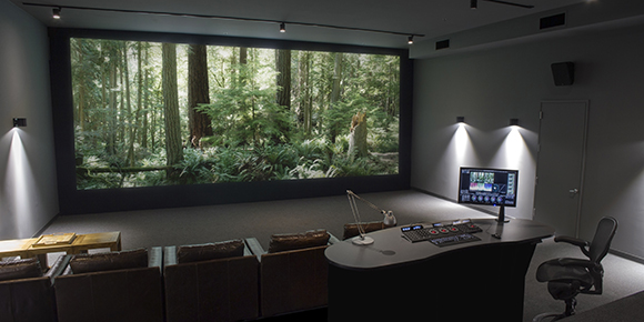 A dark screening room featuring a large screen displaying a forest, leather seating, and a control desk.