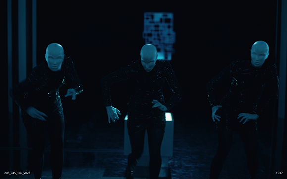 Three pale, bald humanoids in dark, textured clothing crouch in a dark, dimly lit environment.