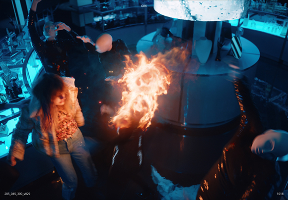 A child in a fur coat stands near mannequins amidst swirling orange flames in a dark, blue-lit setting.