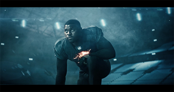 A man in dark athletic clothing crouches in a dimly lit, large stadium.