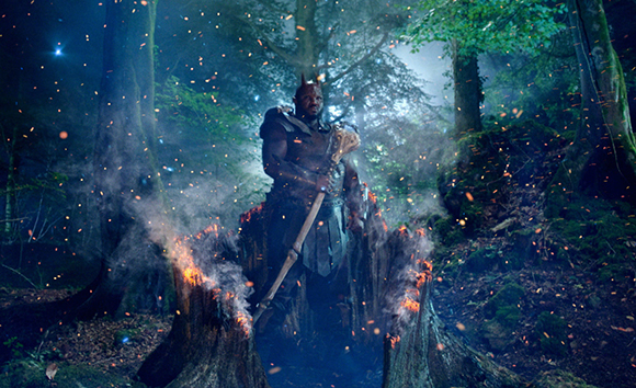 A warrior in dark armor stands in a misty forest surrounded by flying orange sparks and embers.