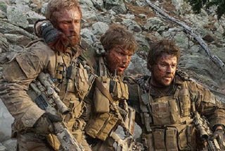 Three soldiers with dirt and blood on their faces move through a rocky, mountainous landscape.