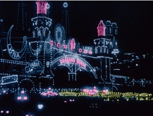 A nighttime view of an amusement park featuring lit-up structures and a sign reading Dragons Gorge.
