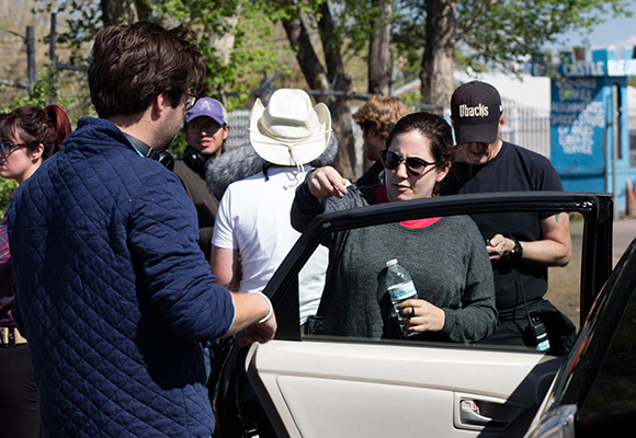 A group of people stand around an open car door on a sunny day.