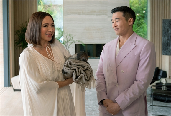 A woman in a white blouse holds a small dog while standing next to a man in a lavender blazer.