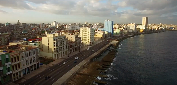Aerial view of a city coastline with multi-story buildings and a road running alongside the ocean.