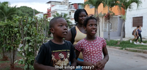 Three Black children stand together outdoors, looking off-camera with curious expressions.