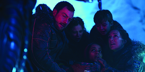 A group of five people with worried expressions huddle together under cool blue lighting.