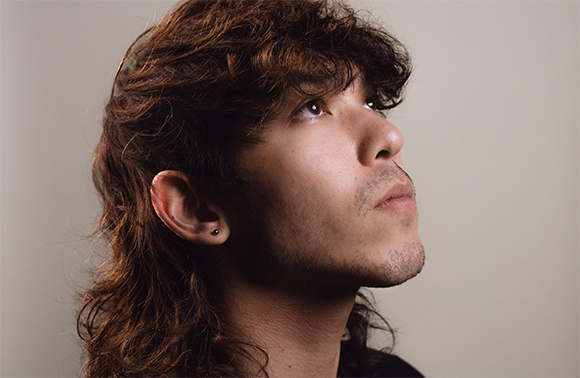 Profile view of a man with wavy brown hair looking up against a neutral background.