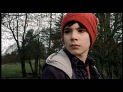 A young person in a red beanie and dark jacket looks forward against a background of bare trees.