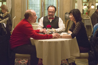 Four people sit around a small table with a white tablecloth in a dimly lit restaurant.