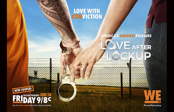 Two people holding hands while handcuffed in front of a prison fence.