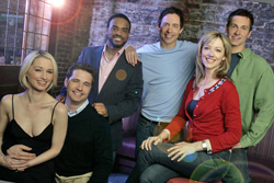 Five smiling adults posing together in a group portrait indoors.