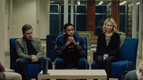 A man in a jacket, a man in a track jacket, and a woman in a black sweater sit in blue armchairs.